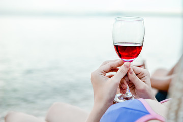 Sexy girl in a swimsuit walking on the beach and holding a glass of wine in hand, on a beautiful sunny day on the weekends.