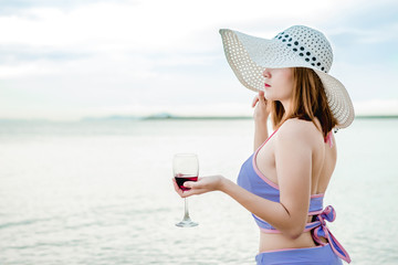 Sexy girl in a swimsuit walking on the beach and holding a glass of wine in hand, on a beautiful sunny day on the weekends.