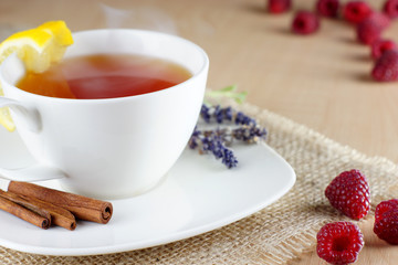 Mug of fruit tea and raspberries on cloth on the table