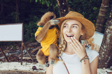 Close up of beautiful young woman with small dress up monkey on her shoulder.  She is smiling and enjoying time with cute little baby monkey on the lonely beach with palm trees.  © anderpe
