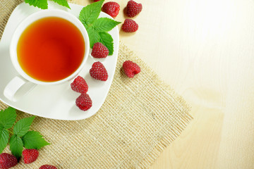 Mug of fruit tea and raspberries on cloth on the table