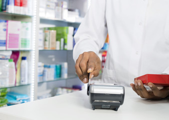Midsection Of Pharmacist Swiping Credit Card While Holding Produ