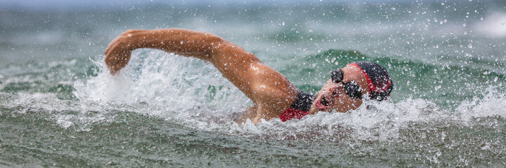 Triathlete man swimming freestyle crawl in ocean panorama banner. Male triathlon swimmer swimming...