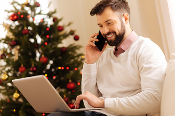 Pleasant man making phone call while using laptop