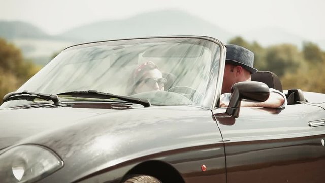 Man gets behind the wheel of a 60s style convertible and talks to his girlfriend