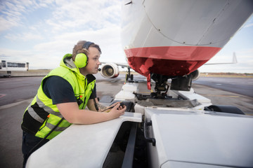 Worker Leaning On Towing Truck With Airplane On Runway