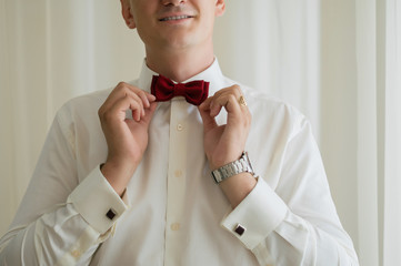 Smiling groom adjusting burgundy bow tie