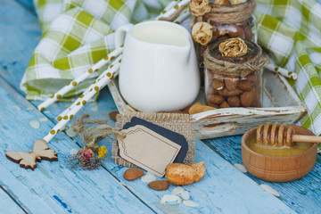 Honey in the wooden bowl, almonds and jar with milk on the wooden tray