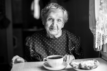 Elderly woman drinking tea in the kitchen, black and white portrait of grandmother.