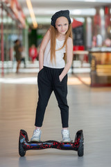 Happy and smiling girl rides on mini segway at trading mall. Teenager riding on hover board or gyroscooter.