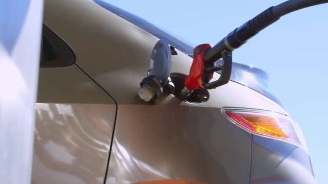 Tracking shot shot of male hand inserting fuel nozzle into opened car tank at gas station at sunny day