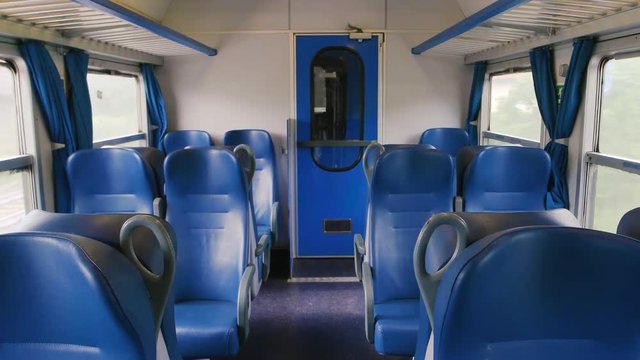 Inside passenger train wagon, day. Train seats and windows, motion.