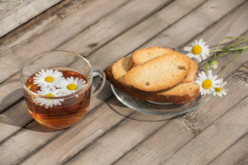 Obraz na płótnie Canvas Herbal tea with daisies and rusks on a glass plate on a wooden table in summer
