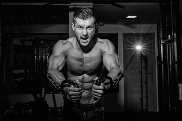 Fototapeta na wymiar Muscular bodybuilder handsome men doing exercises in gym with naked torso. Strong athletic guy with abdominal muscles and biceps. Monochrome image.