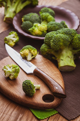 green broccoli on a cutting board with a knife over wooden background