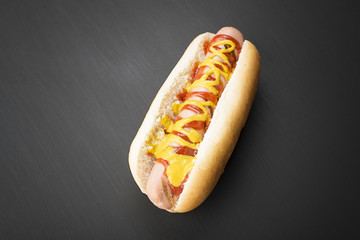 Close-up of hotdog with ketchup and mustard on black background. Fastfood.