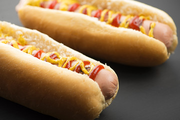 Close-up of two hotdogs with ketchup and mustard on black background. Fastfood.