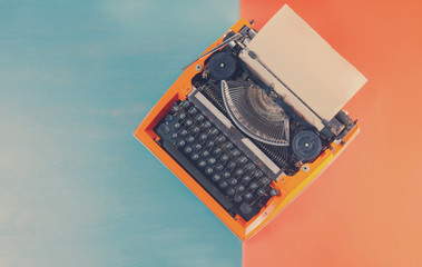 Workspace with orange vintage retro typewriter on blue and orange background, retro background