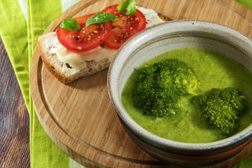 green broccoli vegetable soup and bread with tomato on a rustic wooden table, homemade vegetarian meal  with low calories