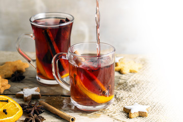 mulled wine in glass mugs with Christmas cookies and spices like orange slices, cloves, star anise and cinnamon on a bright rustic table, background fades to white, copy space