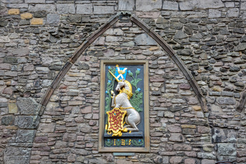 A unicorn with the Scottish flag and an emblem with a red lion on gold on a stone wall