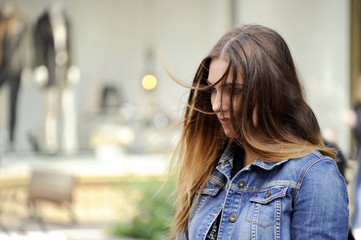 Trendy young hipster woman is looking down sadly with a blowzy hair. City style conception.