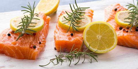 Raw salmon pieces on wooden board with herbs, salt and spices