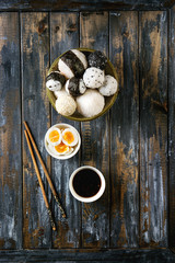 Stone tray with different size rice balls with black sesame and seaweed nori, served with soft boiled eggs, soy sauce, chopsticks over wooden plank background. Asian style dinner. Top view with space