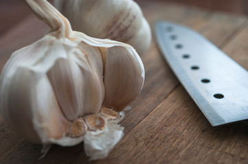 Organic food preparation, cooking concept: raw garlic bulbs heads, knife on a rustic wooden table background