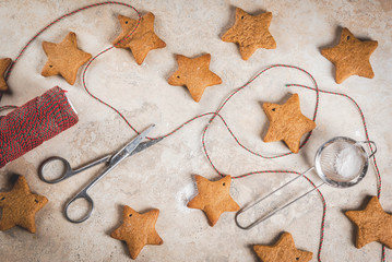 Christmas homemade gingerbread star cookies with sugar powder, green-red decoration rope on light stone background, top view, copy space