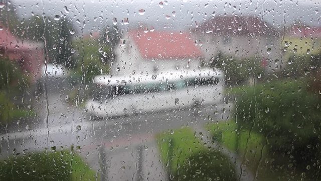 A view from a window in the street on a rainy day, rain drops on the window, blurred cars drive through the road. Handheld footage