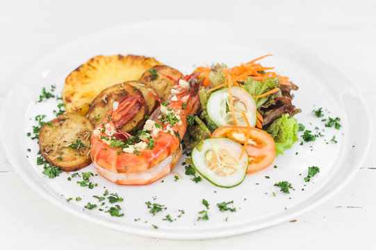Grilled tiger prawn with potatoes, tomatoes and salad on the white plate