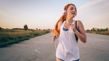 young woman runs and listens to music on headphones on a summer afternoon at sunset