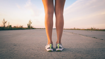 legs of a woman runner on the road close up at sunset