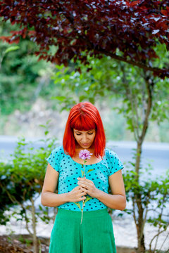 Redhead woman smelling a flower in a park