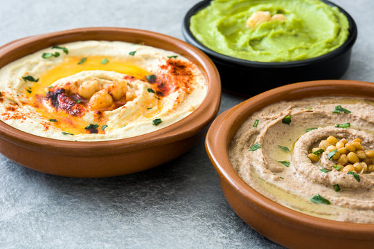 Different hummus bowls. Chickpea hummus, avocado hummus and lentils hummus on gray stone