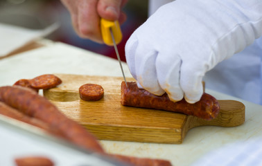Obraz premium man hand slicing sausage with knife