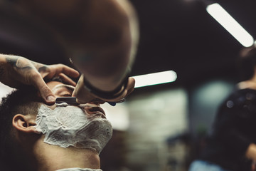 Obraz premium Crop stylish applying foam on customer's cheeks for shaving while working in barbershop.