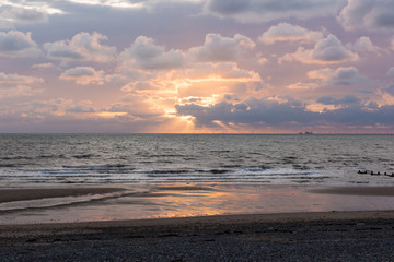A pink and blue creamy cloudy sunset, with sun rays breaking through the clouds. A relaxed quiet sunset evening on the coast.