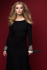 Woman in black dress with a knife in her hand on a red background
