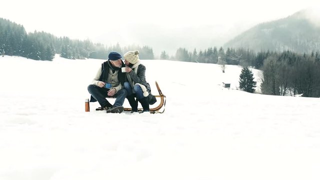 Beautiful senior couple on sledge drinking tea, winter day.