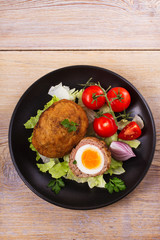Scotch eggs on a plate with cherry tomatoes and salad. View from above, top studio shot, vertical