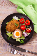 Scotch eggs on a plate with cherry tomatoes and salad. View from above, top studio shot, vertical