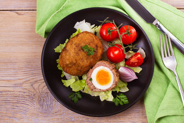 Scotch eggs on a plate with cherry tomatoes and salad. View from above, top studio shot, horizontal