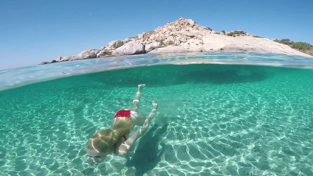 &Upsilon;oung woman swims at the bottom of an exotic beach on half underwater view