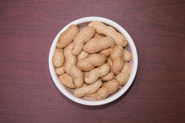 Peanuts uncleaned against a background of brown wood.