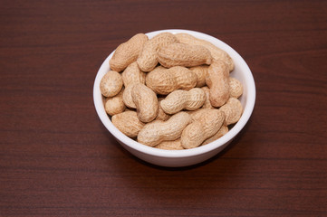 Peanuts uncleaned against a background of brown wood.