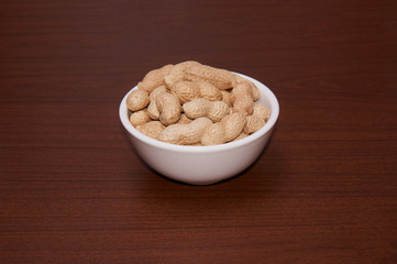 Peanuts uncleaned against a background of brown wood.