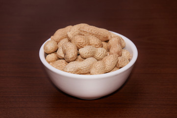 Peanuts uncleaned against a background of brown wood.