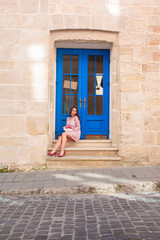 Fototapeta na wymiar Beautiful brunette model in fashionable pink dress holding bouquet of flowers. Woman sitting at the door.
